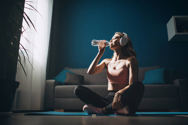 Фитнес-девушка сидит на коврике для йоги и питьевой воде
 - Фото, изображение
