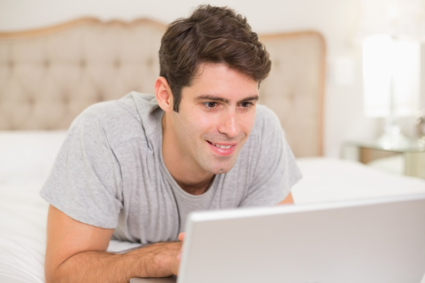 Casual smiling man using laptop in bed - Zdjęcie, obraz