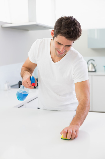 Smiling young man cleaning kitchen counter - Photo, image