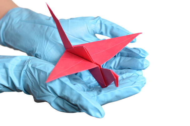 Origami paper crane in hand with rubber gloves over white - Photo, Image