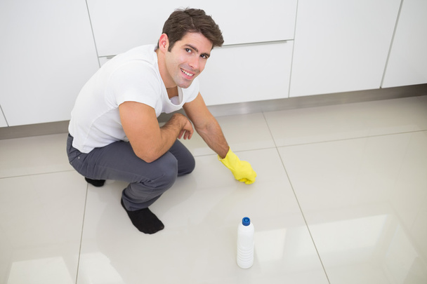 Smiling young man cleaning the kitchen floor - Photo, image