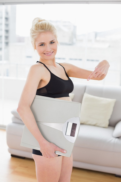 Woman in sportswear carrying scale in fitness studio - 写真・画像