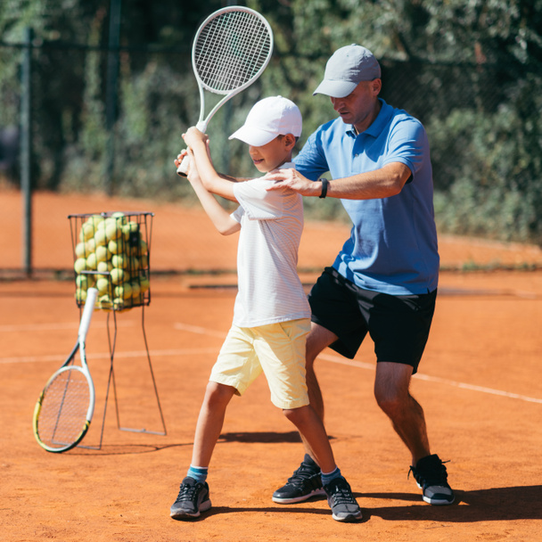 Instructor de Tenis con Joven Talento en Clay Court. Niño teniendo una lección de tenis
. - Foto, imagen