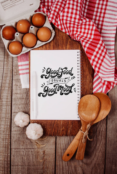 Tagliere in legno su fondo di legno con aglio, mestoli, uova e taccuino bianco con il testo
 - Foto, immagini