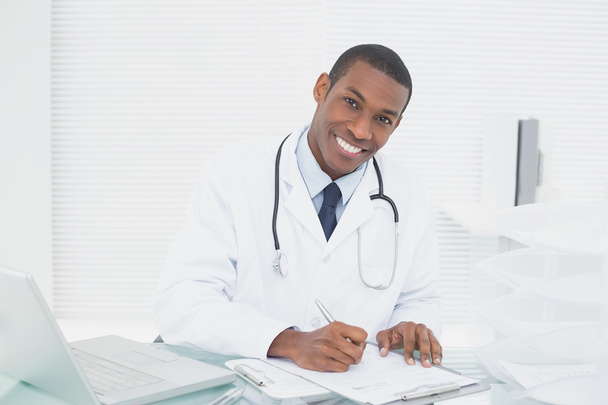 Smiling doctor writing a note at medical office - Foto, immagini
