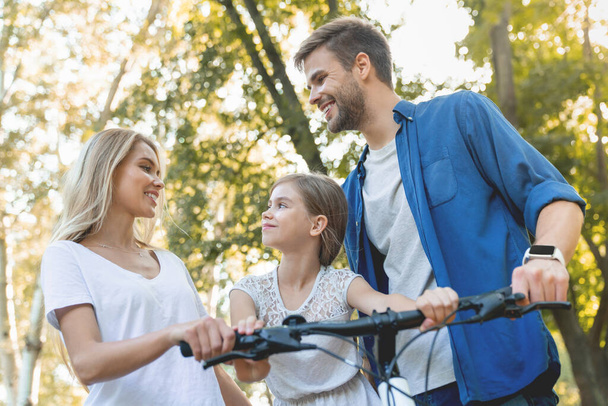 Low angle shot of parents learning their little cute daughter how to ride a bike outdoors - Φωτογραφία, εικόνα