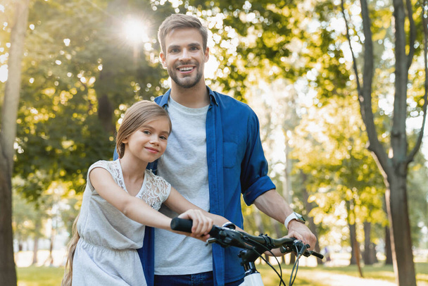 Cute smiling girl learning to ride a bicycle with her father out - Foto, imagen
