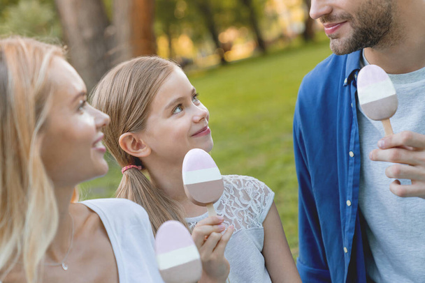 Close up of happy young family eating ice cream and having fun at city park while looking on each other - Photo, Image