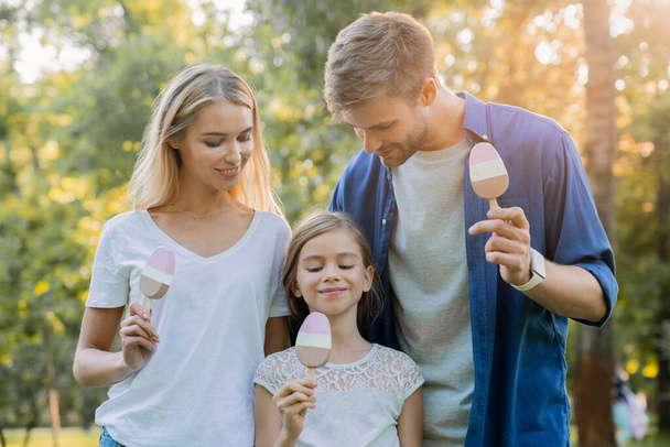 счастливая молодая семья ест мороженое на улице в прекрасный солнечный день в городском парке
 - Фото, изображение