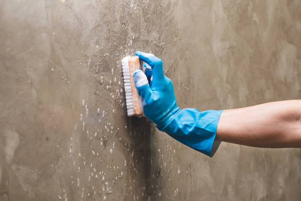 Primo piano mano indossando guanti di gomma blu viene utilizzato per convertire la pulizia scrub sul muro di cemento
. - Foto, immagini