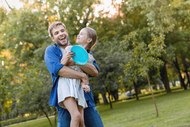 Happy smiling father hugging his smiling pretty daughter with frisby in hands outdoor - Foto, Imagen