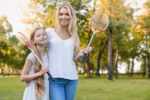 Cute little girl hugging her mother with badminton rackets outdoors - Foto, Imagem