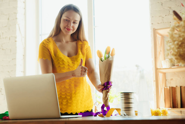 Florist at work: woman shows how to make bouquet with tulips, working at home concept, thumb up - Foto, imagen