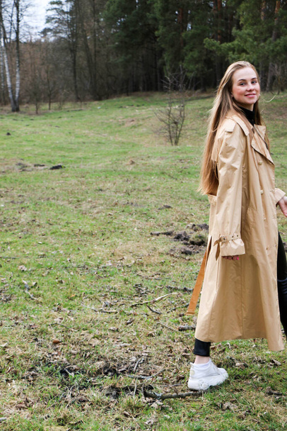 beautiful girl, blonde with long hair, walks in the spring near the forest in a brown coat., serenity and freedom - Фото, изображение