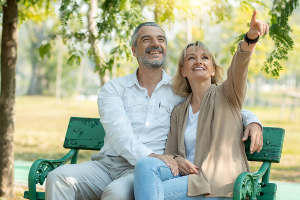 Happy senior couple sit and point to look in park with big smiled - Photo, image