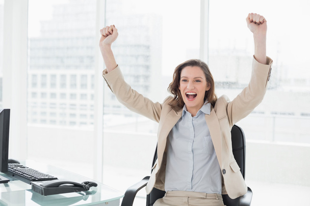Elegant businesswoman cheering with hands raised in office - Foto, afbeelding