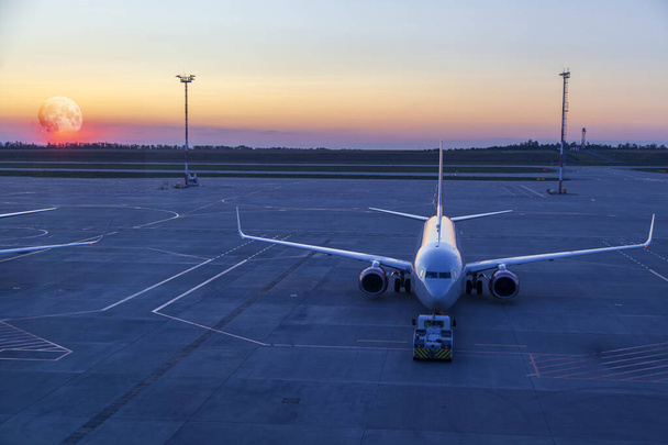 het vliegtuig met de trekker op het vliegveld bij zonsondergang - Foto, afbeelding