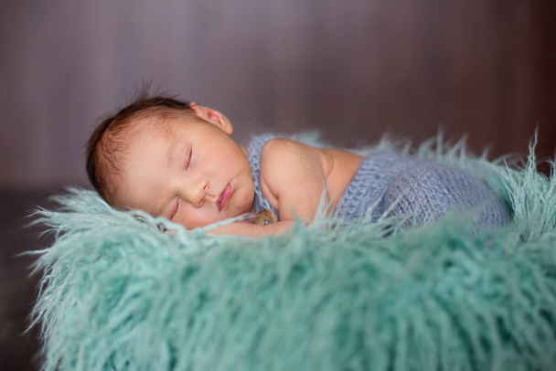 Cute little newborn baby boy, sleeping in basket with colorful wrap - Фото, изображение