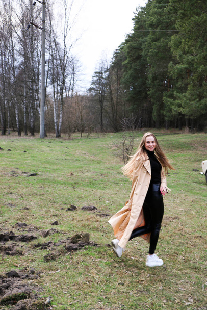 beautiful girl, blonde with long hair, walks in the spring near the forest in a brown coat., serenity and freedom - Zdjęcie, obraz