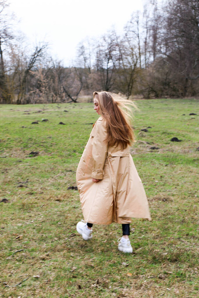 beautiful girl, blonde with long hair, walks in the spring near the forest in a brown coat., serenity and freedom - Foto, Bild