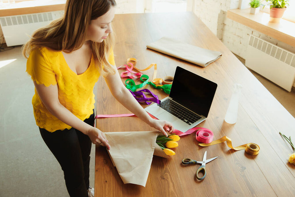 Флорист на работе: женщина показывает, как сделать букет с тюльпанами, работая на дому концепции, с помощью покрытия бумаги
 - Фото, изображение