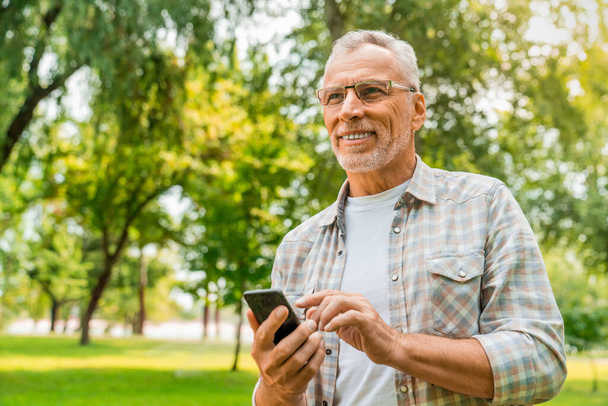 Low angle view of mature man standing outdoors using mobile phone - Photo, image