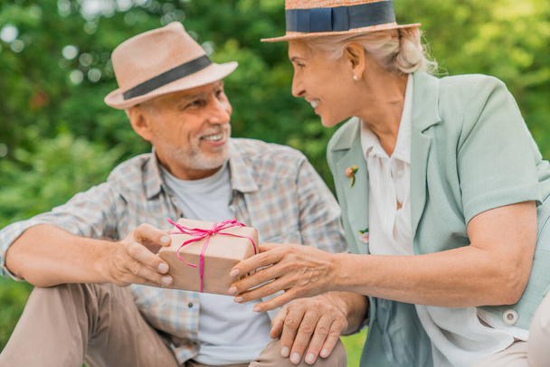Positive senior woman looking at her husband while taking her present from him - Photo, image