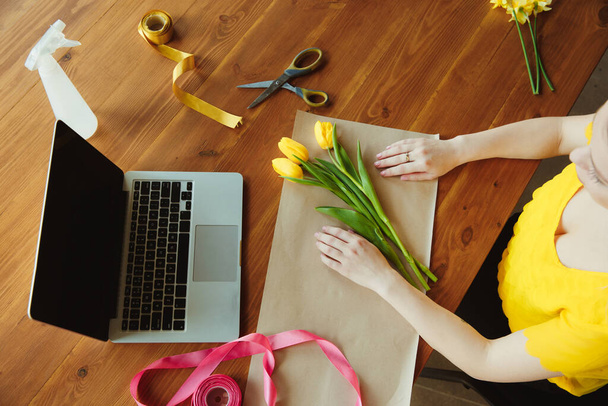 Флорист на работе: женщина показывает, как сделать букет с тюльпанами, работая на дому концепции, вид сверху
 - Фото, изображение