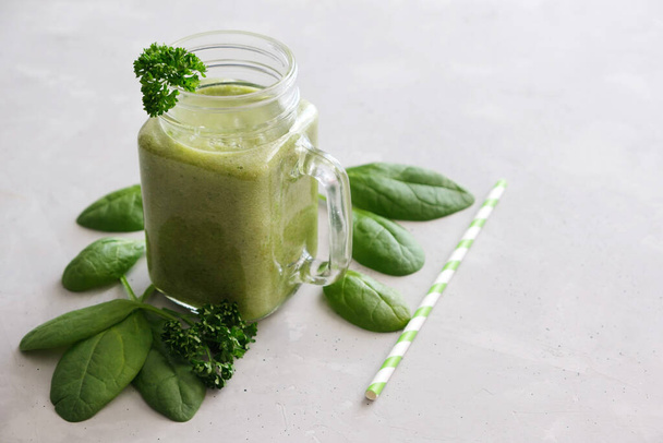 A glass mug, a glass, a glass with a zeon fresh smoothie of banana, apple, celery and spinach with leaves scattered next to it and a reusable straw on a gray concrete background. Healthy snack. - Photo, image