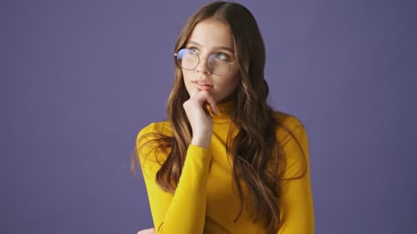 A thoughtful teenage girl is dreaming about something and come up with an idea standing isolated over a purple background in studio - Materiaali, video