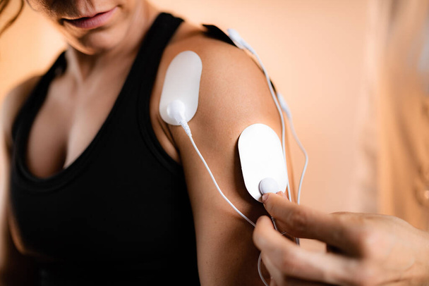Shoulder Physical Therapy with TENS Electrode Pads, Transcutaneous Electrical Nerve Stimulation. Therapist Positioning Electrodes onto Patient's Shoulder - Photo, Image