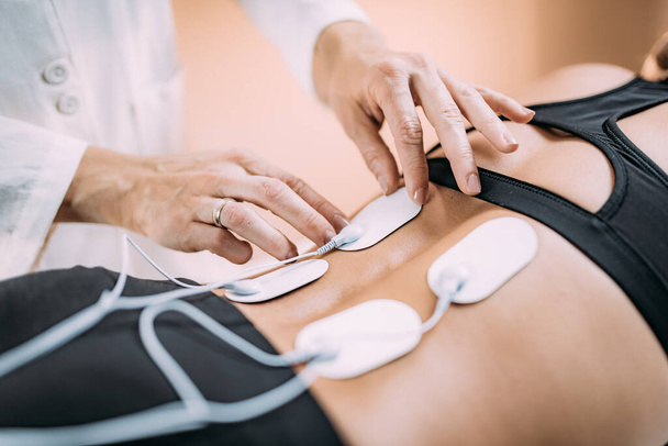 TENS電極パッド、経皮的電気神経刺激による腰痛物理療法。患者の腰に電極を配置するセラピスト - 写真・画像