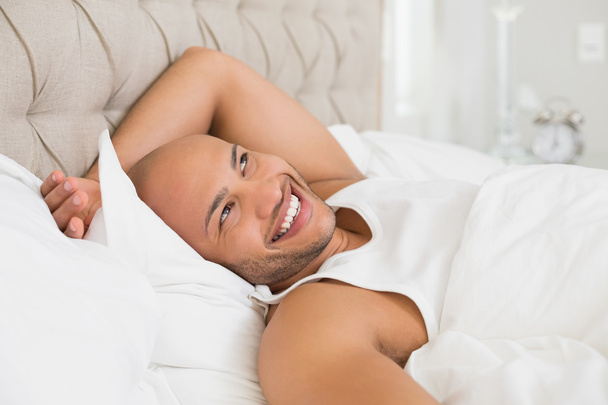 Smiling young bald man resting in bed - 写真・画像