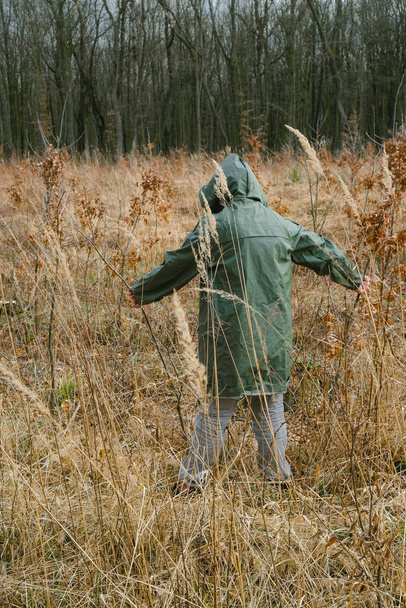  Een scène van angst en paniek in een catastrofe. Een eenzame gemiddelde persoon in beschermende kleding gaat ergens heen. Droog gras en bomen in het bos. - Foto, afbeelding