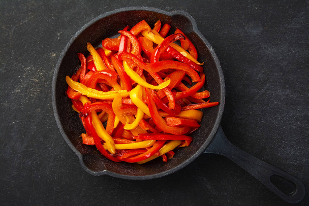 μαγειρεμένα λαχανικά σε μαύρο πιάτο και σκούρο φόντο, κόκκινο και κίτρινο πιπέρι - Φωτογραφία, εικόνα