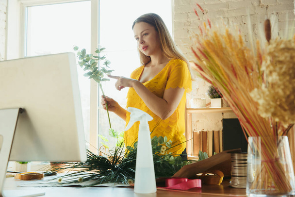 Florist at work: woman shows how to make bouquet, working at home concept, choosing plants for composition - Photo, Image