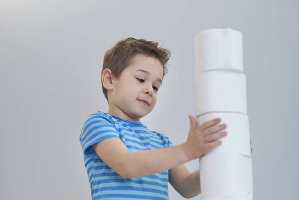 A fiú vécépapírt épít. Aktív fiú játszik WC-papírral retro szűrőben. A gyerek megölel egy csomó WC-papírt, a gyerekek egészségügyi koncepciója - Fotó, kép