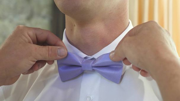 close-ups of a man s handles corrects a blue bow tie. man dresses bow tie on white shirt. Man getting dressed for party. stylish gentleman. fashionable stylish businessman. fashion and style concept - Фото, изображение
