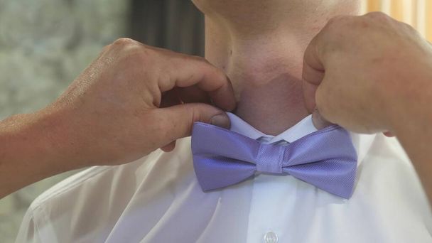 close-ups van een mannenhandvat corrigeert een blauwe vlinderdas. man kleedt strikje op wit shirt. Een man die zich aankleedt voor het feest. Stijlvolle heer. modieuze stijlvolle zakenman. mode- en stijlconcept - Foto, afbeelding