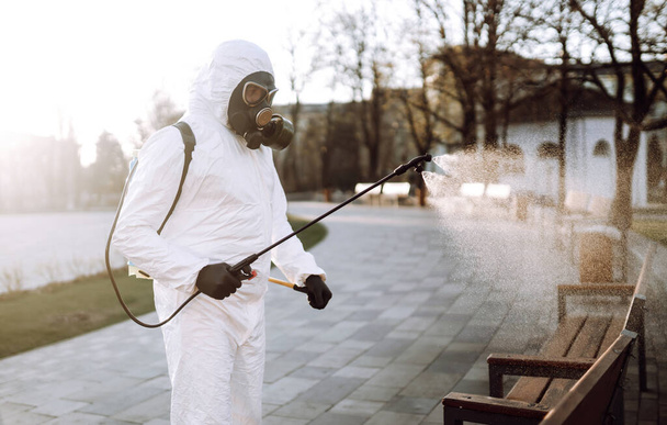 Man in virus protective suit and mask disinfects public places  with spray chemicals to prevent the spreading of the coronavirus. Infection prevention and control of epidemic. Covid-19. - Фото, изображение