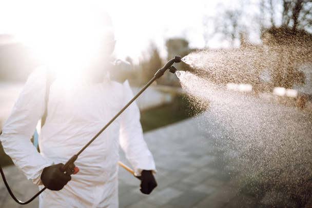 Man in virus protective suit and mask disinfects public places  with spray chemicals to prevent the spreading of the coronavirus. Infection prevention and control of epidemic. Covid-19. - 写真・画像