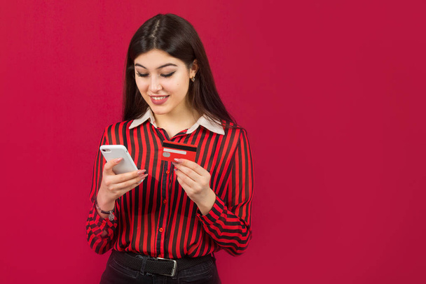 beautiful young woman with credit card and phone on a red background - Photo, Image