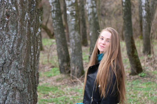 beautiful girl, blonde with long hair, walks in the spring near the forest in a brown coat - Fotoğraf, Görsel