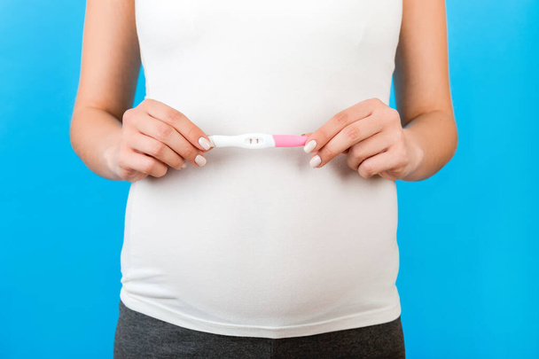 Immagine ritagliata di donna incinta in abbigliamento domestico che mostra un test di gravidanza positivo con due strisce su sfondo blu. Gravidanza sana. Copia spazio
. - Foto, immagini