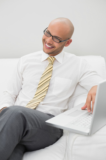 Businessman using laptop on sofa at home - Фото, изображение