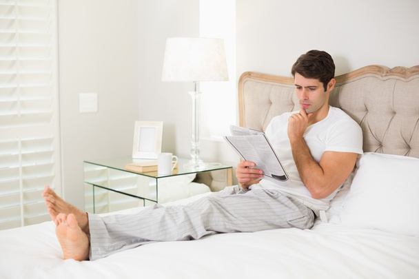 Casual man reading newspaper in bed - Фото, изображение