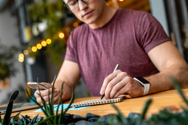 Schnappschuss eines jungen konzentrierten Geschäftsmannes mit Smartphone und Notizen beim Coworking - Foto, Bild