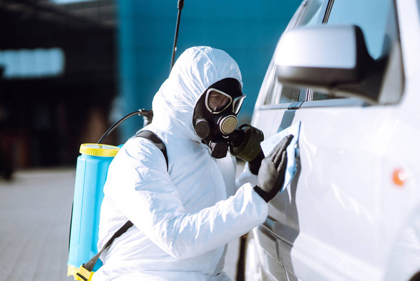 Man in protective suit washing and disinfection handles of a car, to preventing the spread of the epidemic of coronavirus, pandemic in quarantine city. Covid-19. - Fotó, kép