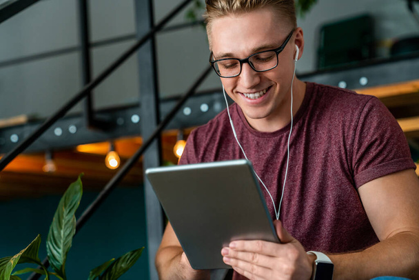 Young smiling man using digital tablet and headphones in the office - Foto, Bild