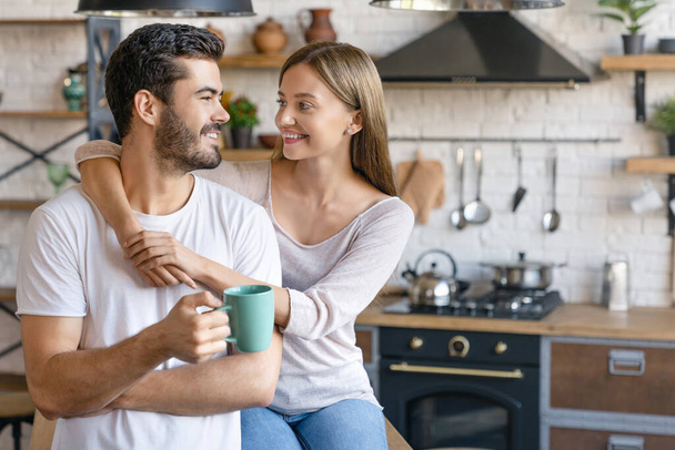 Beautiful young couple embracing in the kitchen at home with look on each other - Foto, Bild